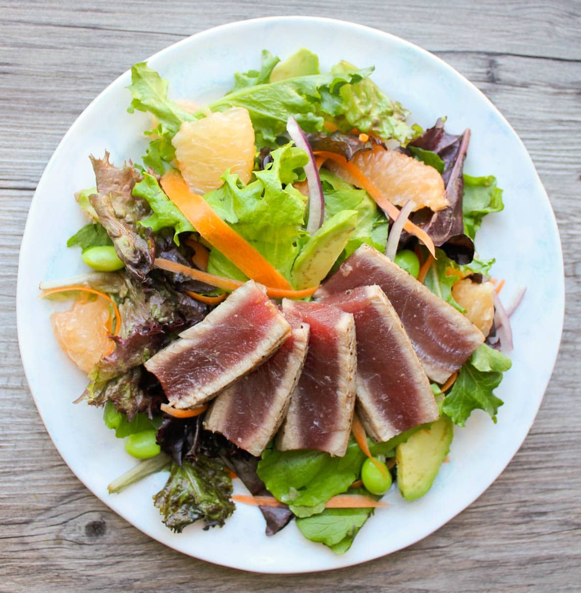 Overhead view of rare seared ahi tuna fanned over greens with carrots, grapefruit, avocado, and edamame.