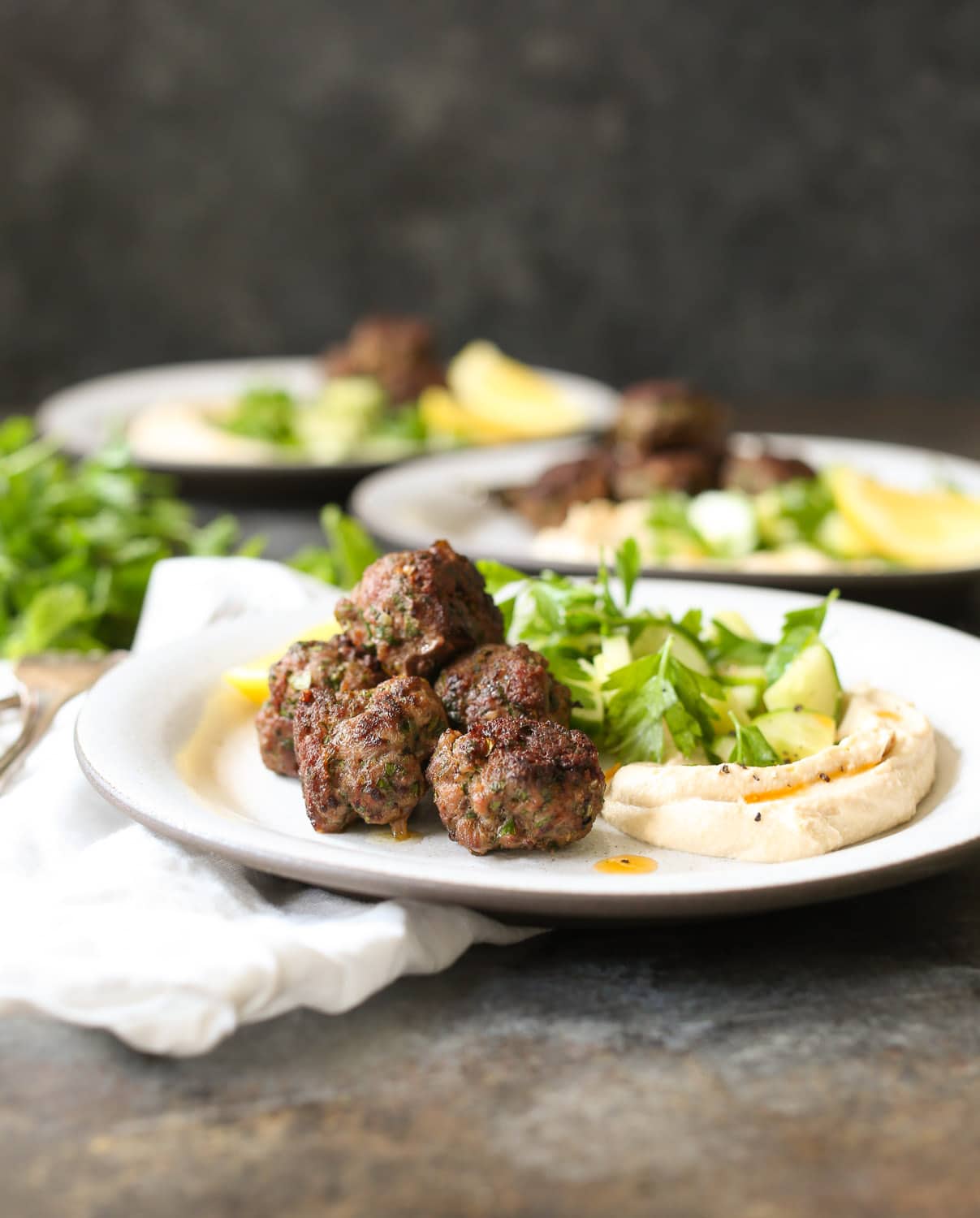 Close up of lamb kofta with hummus and cucumber salad with fresh herbs.