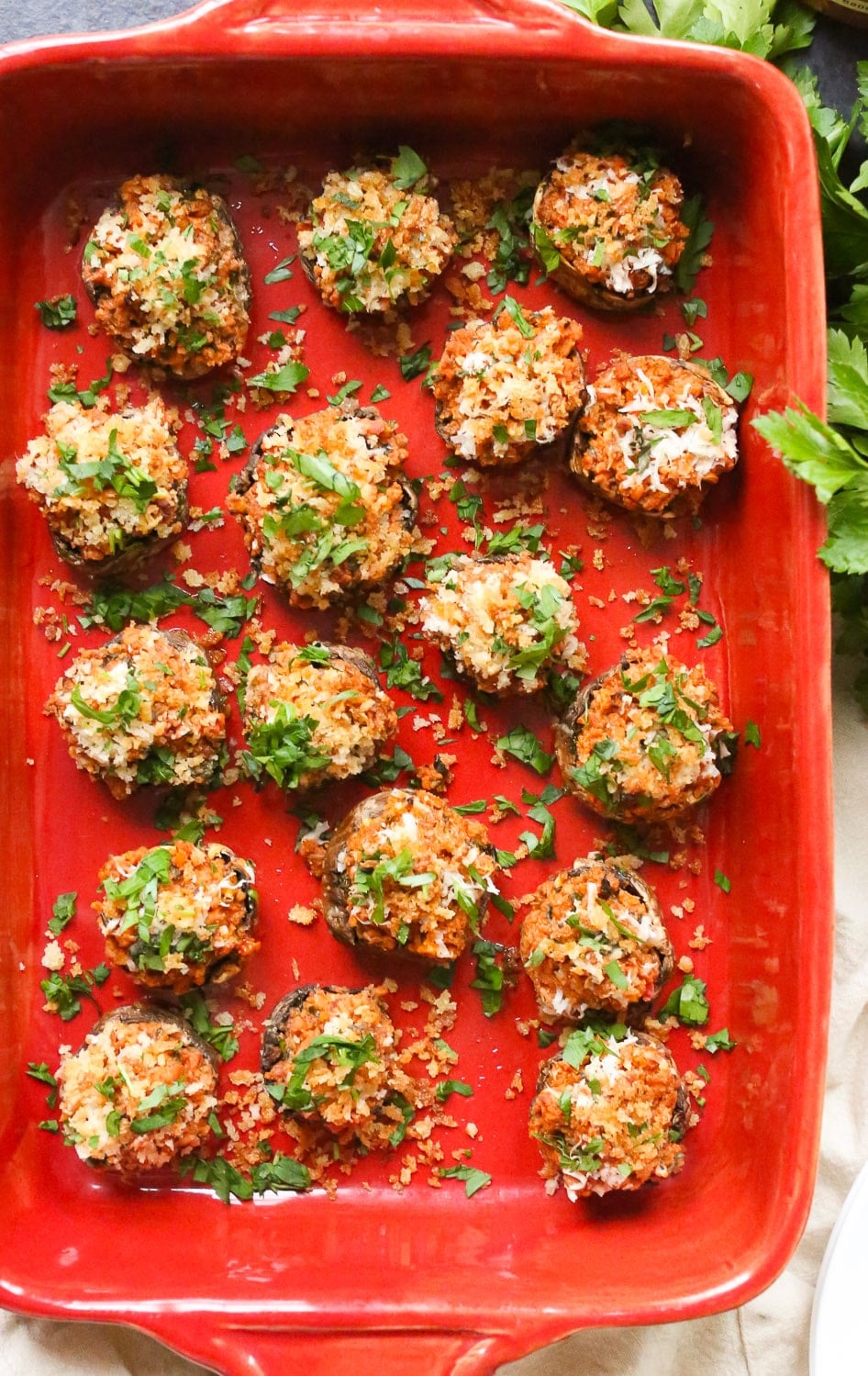 Overhead closeup of a full baking dish of stuffed mushrooms topped with chopped parsley.